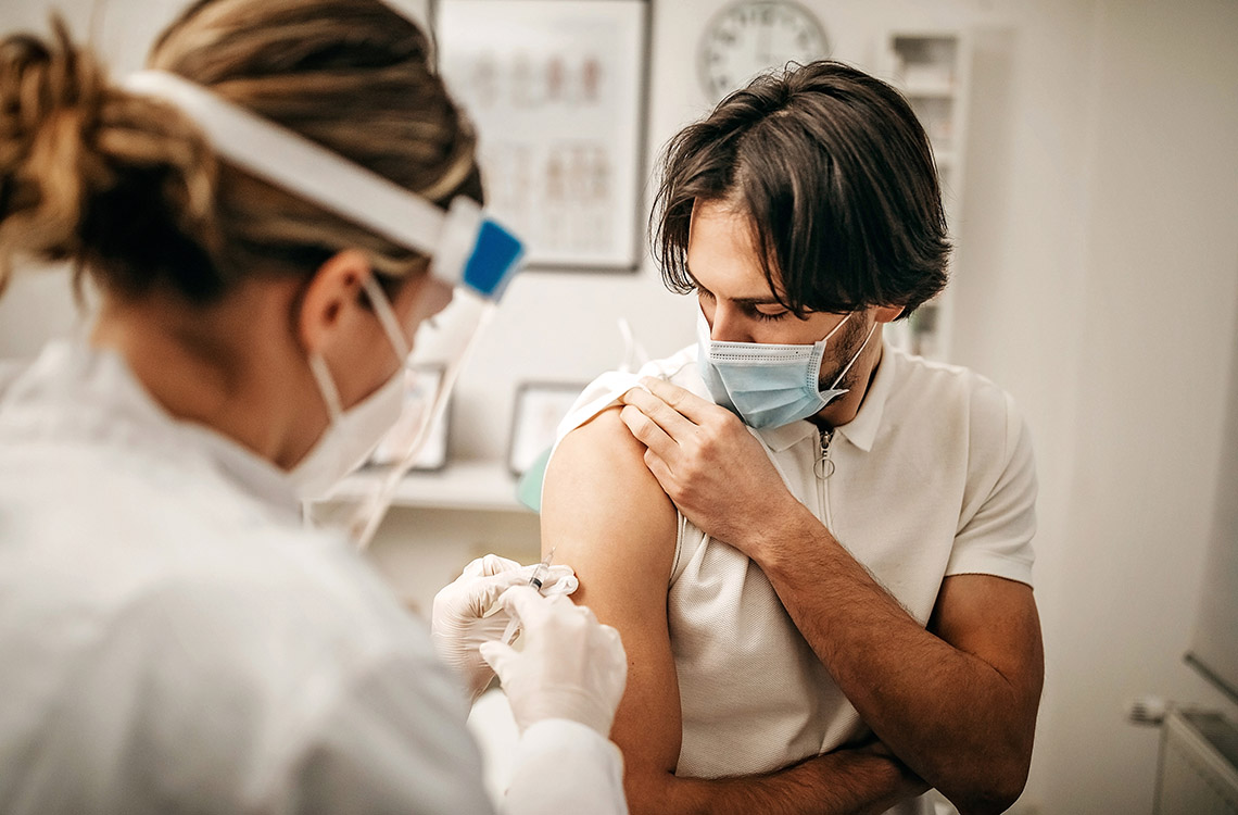 Hoitaja antaa rokotteen miehen käsivarteen.