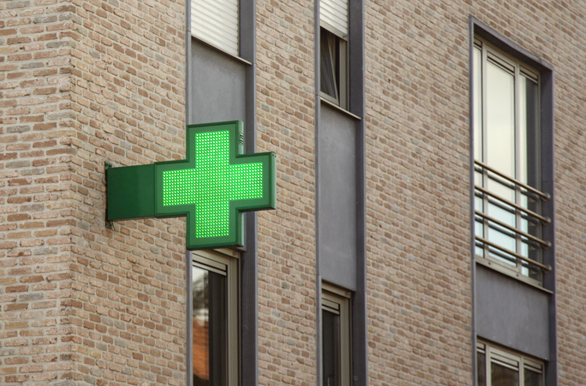 Kuvassa on vihreä apteekin logo rakennuksen seinässä.